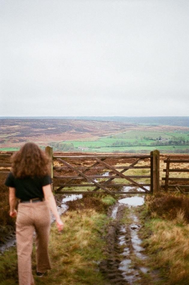 woman walking towards a gate with the Yorkshire country scenery in the background.