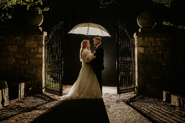 Bride and groom in darkness, holding unbrella, bride wears furry coat